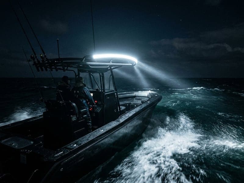 Rampe LED incurvée allumée sur un bateau de pêche en navigation de nuit, faisceau panoramique puissant éclairant la mer agitée