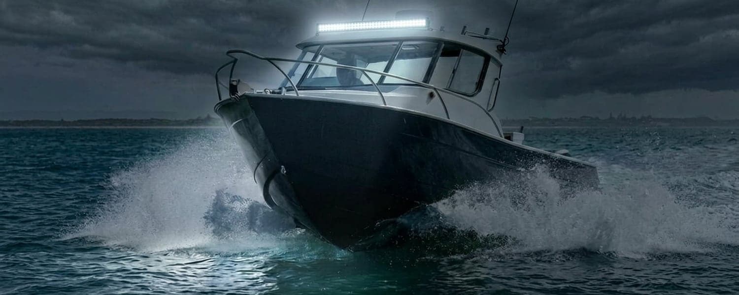 Barre LED étanche pour milieu marin allumée sur un bateau en navigation de nuit, faisceau puissant éclairant l'océan et les embruns
