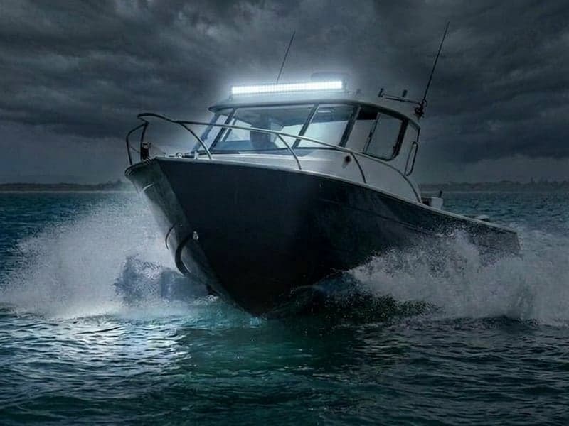 Barre LED étanche pour milieu marin allumée sur un bateau en navigation de nuit, faisceau puissant éclairant l'océan et les embruns