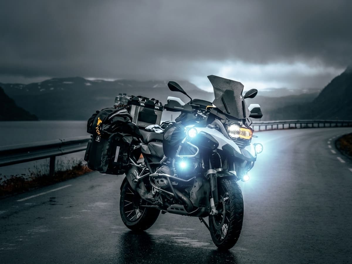 Phares LED additionnels allumés sur une moto trail BMW R1200GS de nuit sur la route, faisceau puissant éclairant, vue de 3/4