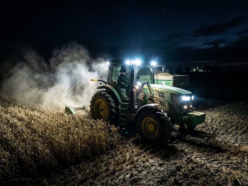 Tracteur agricole travaillant de nuit avec phares LED Next-Tech puissants éclairant un champ de maïs poussiéreux