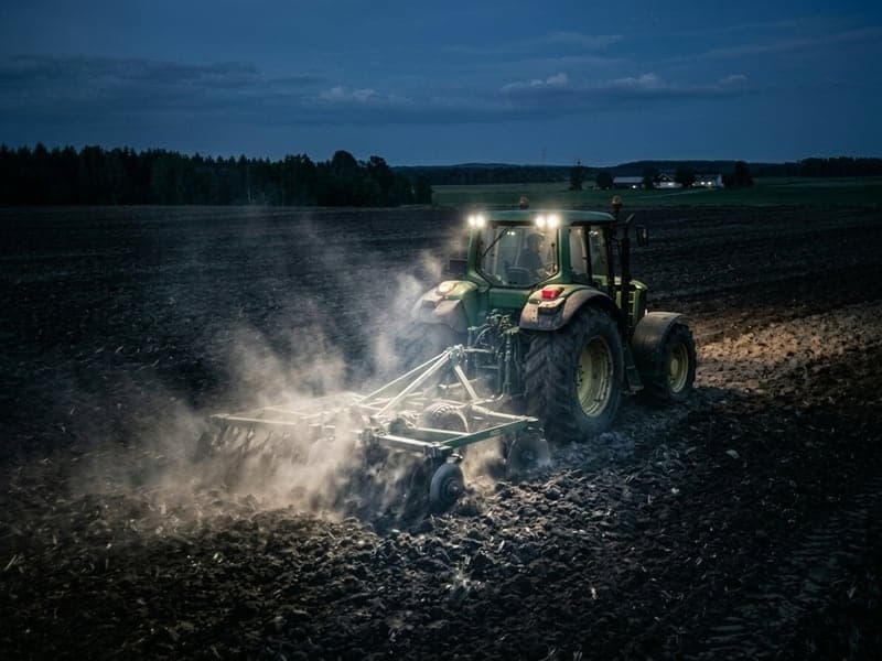 Tracteur agricole équipé de phares LED Next‑Tech déchaumant un champ de nuit, projecteurs allumés et poussière soulevée, vue de derrière