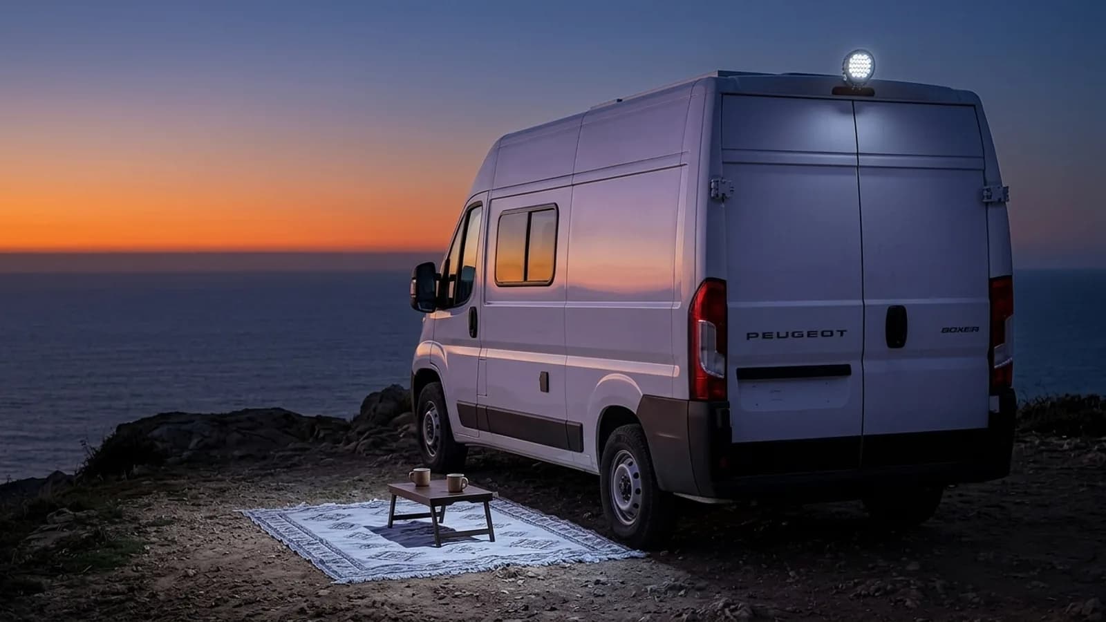Peugeot Boxer aménagé en soirée au bord de l'océan, phare LED Next-Tech éclairant le campement