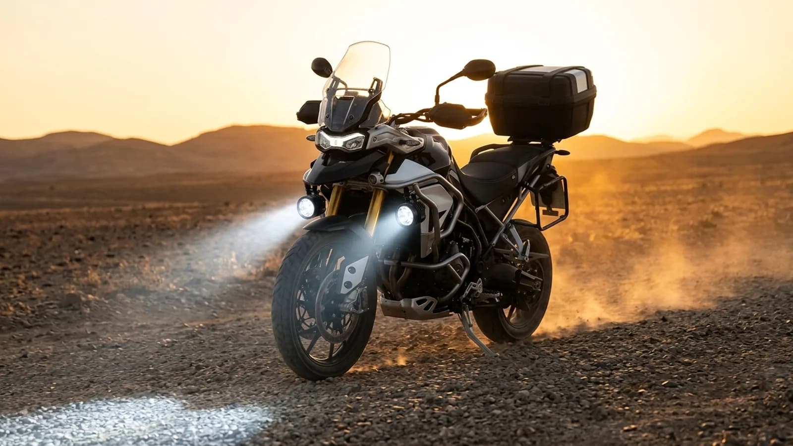 Triumph Tiger 900 sur piste de gravier au coucher du soleil, feux additionnels LED Next-Tech allumés