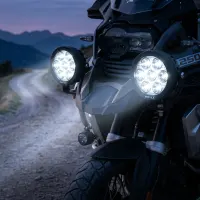 kit de feux LED ronds Next‑Tech XP7 140w 18800 lumens 5000K allumés sur une moto en montagne au crépuscule