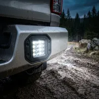 Feu LED de recul Next‑Tech encastré dans le pare-chocs arrière d'un 4x4, allumé en blanc sur piste boueuse au crépuscule
