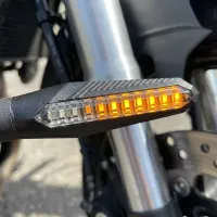 Zoom sur un clignotant LED séquentiel Next‑Tech orange allumé monté sur la fourche chromée d'une moto