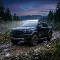 pick-up Ford Ranger Raptor noir de 3/4 sur piste boueuse au crépuscule équipé d'une barre LED Next‑Tech incurvée allumée blanc pur
