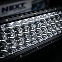 gros plan sur les lentilles réflecteurs centrales d'une barre LED Next‑Tech incurvée éteinte, boîtier alu noir et logo en arrière-plan