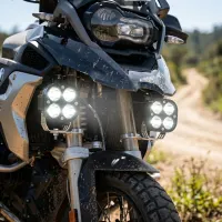 gros plan sur une moto trail équipée de feux LED longue portée carrés Next‑Tech allumés blanc pur, sur piste tout-terrain