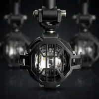 gros plan sur un feu LED antibrouillard Next‑Tech pour moto avec grille de protection noire et lentille blanc pur, sur fond sombre