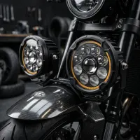 gros plan sur deux phares LED ronds 120mm Next‑Tech éteints montés sur une moto café racer à garde-boue carbone dans un garage