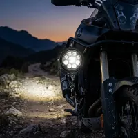 gros plan sur un phare LED rond 90w Next‑Tech monté sur moto trail au crépuscule, faisceau blanc éclairant un sentier rocailleux