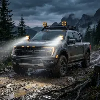 pick-up ford raptor de 3/4 sur piste boueuse de montagne équipé de feux LED carrés Next‑Tech, faisceaux blancs allumés sous la pluie