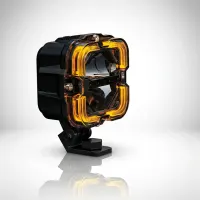 feu LED carré 100mm Next‑Tech avec cache jaune ambré et support de fixation, sur fond studio blanc en vue de 3/4