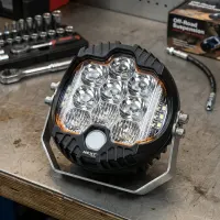 Projecteur LED rond Next‑Tech120mm posé sur un établi d'atelier, vue de face éteint