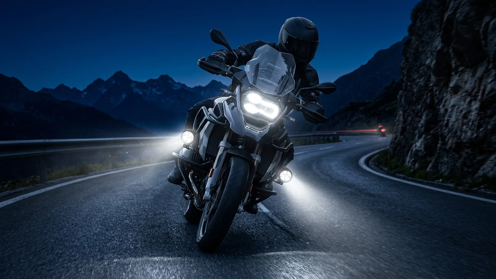 Moto de nuit en virage avec feux additionnels longue portée allumés sur route de montagne